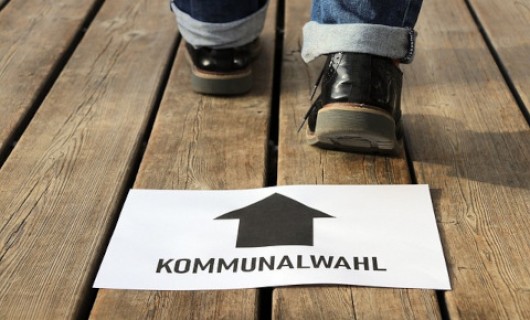 Schild mit Aufschrift &quotKommunalwahlen&quot vor zwei sich nach vorn bewegenden Füßen